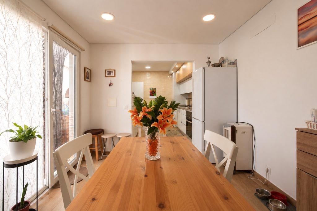 Mesa de refeições junto à porta envidraçada para o pátio, com a cozinha ao fundo, moradia no Barreiro